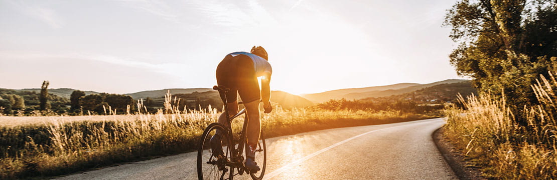 Cyclist rides on a rural road at sunset.